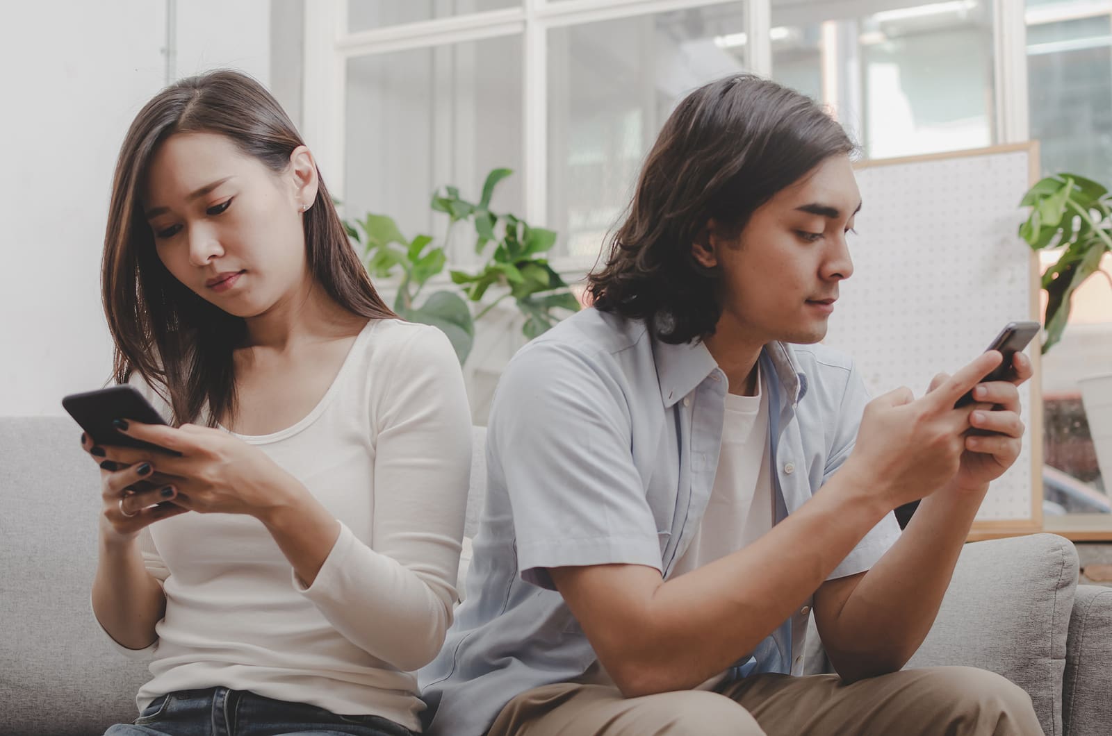 A man and woman sitting on the couch looking at their phones.