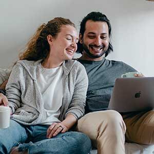 A man and woman sitting on the couch looking at a laptop.