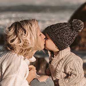 A woman and child kissing on the beach.